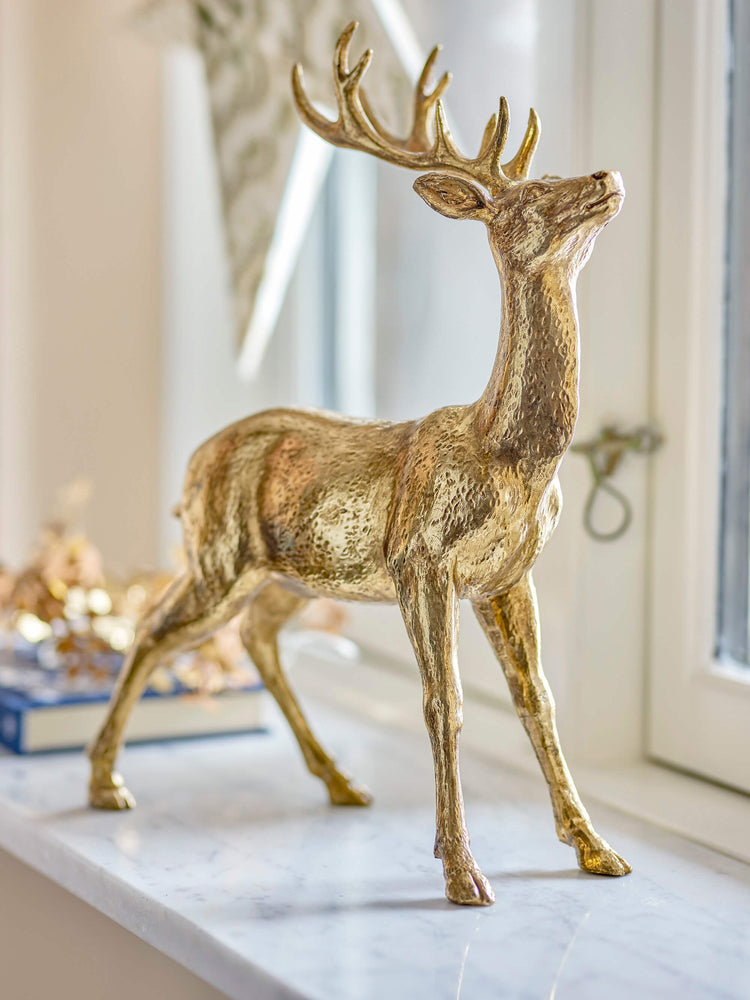 Keera Deer by Bloomingville beautifully displayed on a windowsill with small decorative trees and candlesticks. The golden polyresin deer adds a touch of elegance to your Christmas decor. Size: 36.5cm(H) x 27cm(L) x 11cm(W).