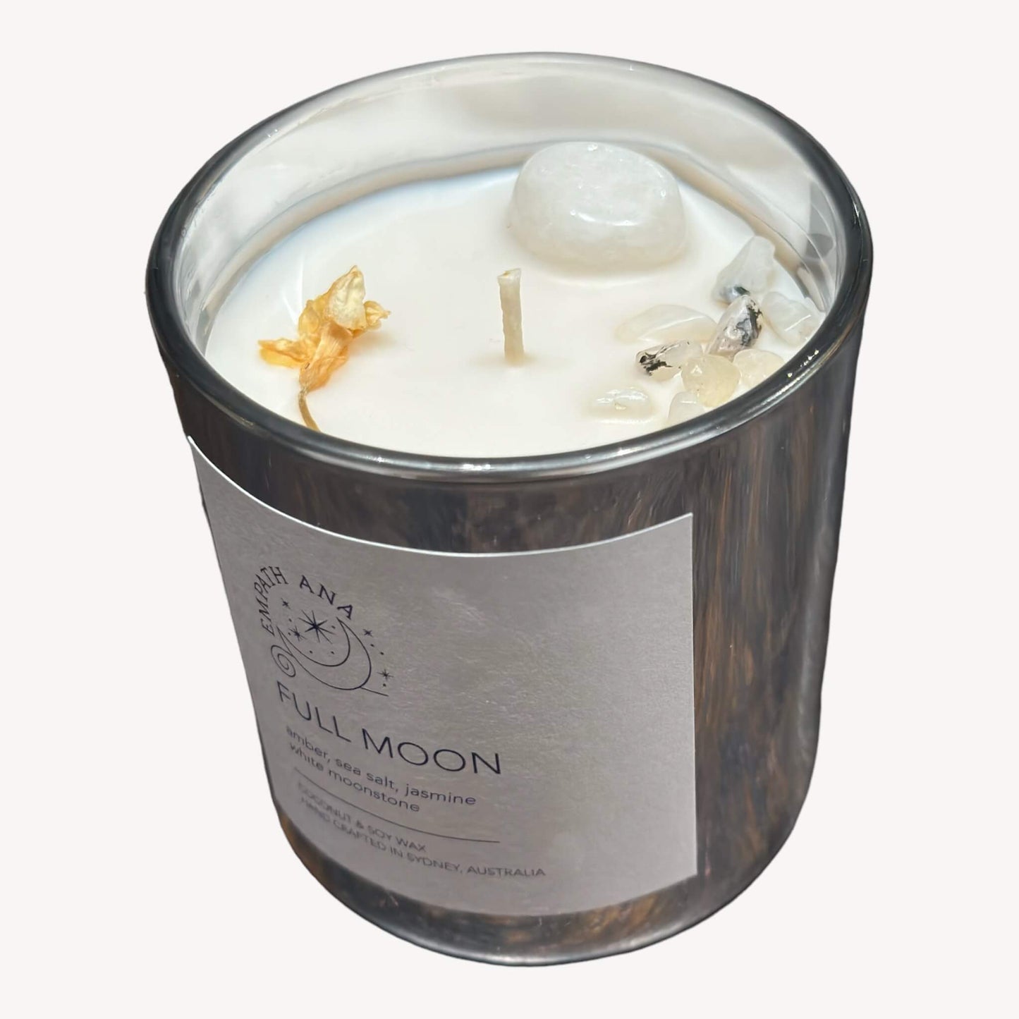 Top view of Empath Ana's Full Moon Crystal Candle in the Medium size (200mls). Ethereal White/Rainbow Moonstone crystals adorn the top, enhancing the celestial energy. The invigorating blend of Amber, Sea Salt, and Jasmine invites you to contemplate and celebrate joyous moments.