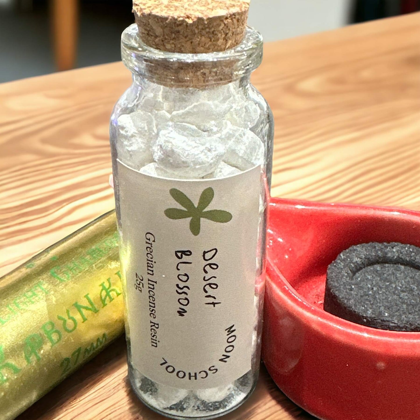 Bottle of Grecian Desert Blossom Incense Resin elegantly placed on a bench, accompanied by an incense burner ceramic dish and a roll of Easy-Light Charcoals. Crafted with excellence, this A Grade quality resin envelops your space in a fragrant embrace, creating an inviting ambiance of tranquility and charm.