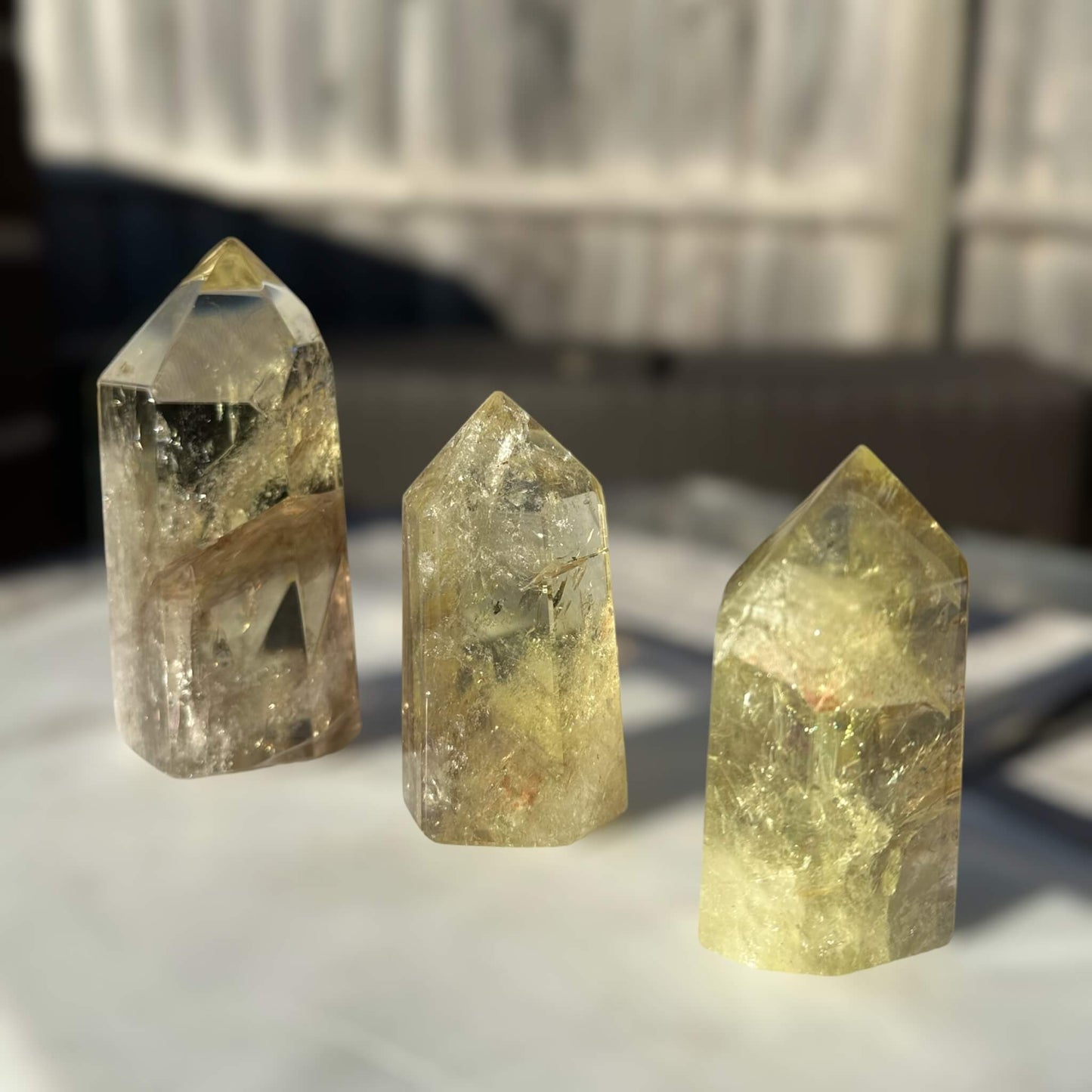 Three Lemon Smoky Quartz Crystal Generators - varying in sizes of 10cm, 7.5cm and 7.3cm high. Each crystal exhibits unique formations and shades, creating a captivating display.